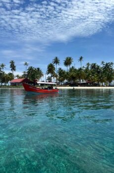 Embarcación llegando a Isla Pelícano, rodeada de aguas cristalinas y palmeras.