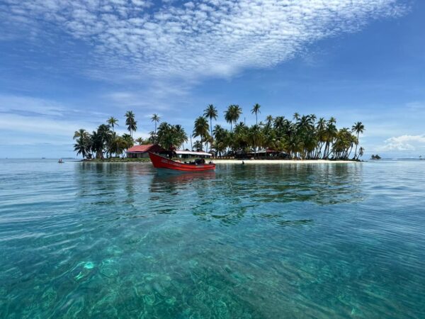 Embarcación llegando a Isla Pelícano, rodeada de aguas cristalinas y palmeras.